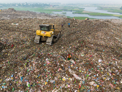 Aminbazar Bangladesh 26 January 2025 Aerial view of a yellow bulldozer moving waste at the Aminbazar landfill with workers scavenging among piles of garbage near a river. Aminbazar Bangladesh 26 January 2025 Aerial view of a yellow bulldozer moving waste at the Aminbazar landfill with workers scavenging among piles of garbage near a river.