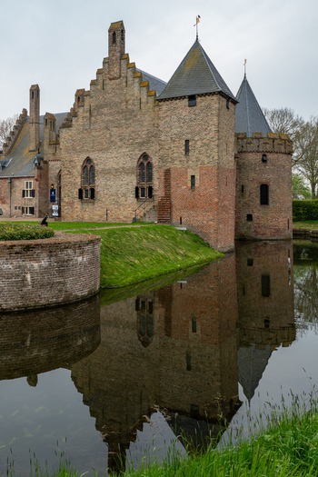 View of Radboud Castle with its medieval brick walls and towers reflecting in the calm water of the surrounding moat under an overcast sky in Medemblik Noord Holland Netherlands. View of Radboud Castle with its medieval brick walls and towers reflecting in the calm water of the surrounding moat under an overcast sky in Medemblik Noord Holland Netherlands.