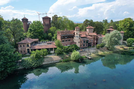 Aerial view of the Borgo Medievale historic complex situated along the riverbank surrounded by lush green trees and summer foliage in Torino Piemonte Italy.