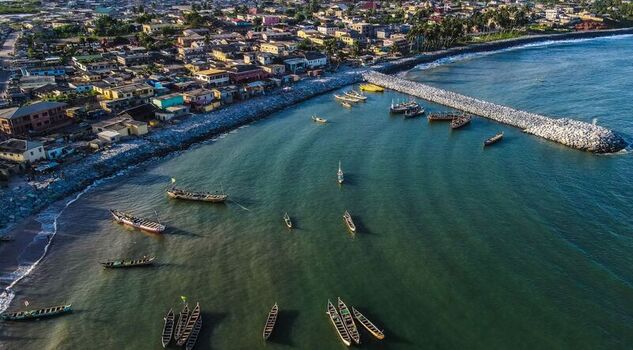 Aerial view of traditional wooden fishing boats moored in a calm bay near a stone breakwater and a coastal town in Ghana. Aerial view of traditional wooden fishing boats moored in a calm bay near a stone breakwater and a coastal town in Ghana.
