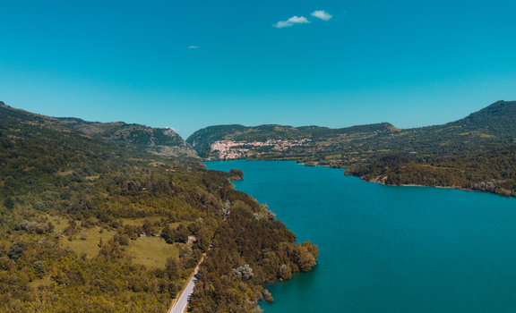Aerial view of Lago di Barrea surrounded by lush green hills and dense forests under a clear blue sky in Province of L Aquila Abruzzo Italy.