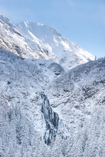 View of the Transfagarasan mountain pass featuring a frozen waterfall cascading down snow covered rocky slopes surrounded by dense pine forests in Curtea de Arges Judetul Arges Romania. View of the Transfagarasan mountain pass featuring a frozen waterfall cascading down snow covered rocky slopes surrounded by dense pine forests in Curtea de Arges Judetul Arges Romania.