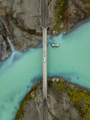 Aerial view of a bridge crossing a turquoise glacial river with a white car driving across surrounded by the rugged volcanic terrain of Kerlingarfjoll in Hrunamannahreppur Iceland. Aerial view of a bridge crossing a turquoise glacial river with a white car driving across surrounded by the rugged volcanic terrain of Kerlingarfjoll in Hrunamannahreppur Iceland.