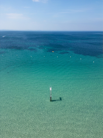 Aerial view of the turquoise sea with a marker pole in the clear water under a blue sky in Trebeurden Brittany France. Aerial view of the turquoise sea with a marker pole in the clear water under a blue sky in Trebeurden Brittany France.