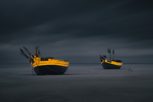 View of two yellow and black fishing boats resting on a sandy beach under a dark overcast sky in Debki Pomeranian Voivodeship Poland. View of two yellow and black fishing boats resting on a sandy beach under a dark overcast sky in Debki Pomeranian Voivodeship Poland.