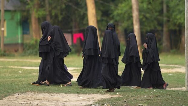 View of women in black niqabs walking across a field Bangladesh.