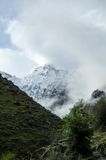 View of the snow capped Nanga Parbat mountain partially obscured by clouds rising above a rocky green covered slope in Jaglot Gilgit Pakistan. View of the snow capped Nanga Parbat mountain partially obscured by clouds rising above a rocky green covered slope in Jaglot Gilgit Pakistan.