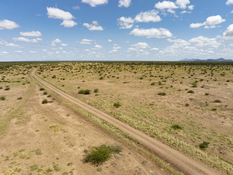 Aerial view of a dirt road winding through the arid landscape of the savanna with sparse shrubs and scattered acacia trees under a bright blue sky Marsabit County Kenya. Aerial view of a dirt road winding through the arid landscape of the savanna with sparse shrubs and scattered acacia trees under a bright blue sky Marsabit County Kenya.
