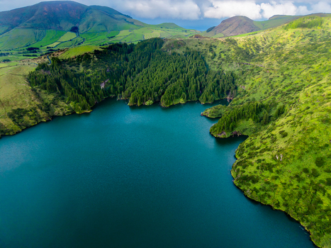 Aerial view of the deep blue lake waters contrasting with the vibrant green of the surrounding hills and dense forest Flores Azores Portugal.