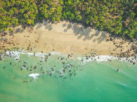 Aerial view of Cabo de Rama Beach with turquoise ocean waves sandy shoreline rocky coast and lush palm trees in Canaguinim Goa India.