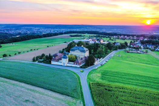 Aerial view of Schloss Jagersburg surrounded by green fields and a village at sunset in Eggolsheim Bayern Germany.