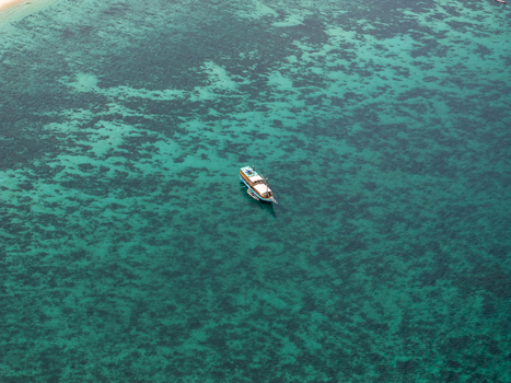 Aerial view of a wooden boat floating in the turquoise waters of Komodo National Park with coral reefs visible beneath the surface in Komodo East Nusa Tenggara Indonesia. Aerial view of a wooden boat floating in the turquoise waters of Komodo National Park with coral reefs visible beneath the surface in Komodo East Nusa Tenggara Indonesia.