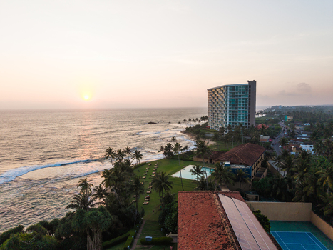 Aerial view of a coastal resort featuring a high rise hotel swimming pool and palm trees along the beach at sunset in Galle Southern Province Sri Lanka. Aerial view of a coastal resort featuring a high rise hotel swimming pool and palm trees along the beach at sunset in Galle Southern Province Sri Lanka.