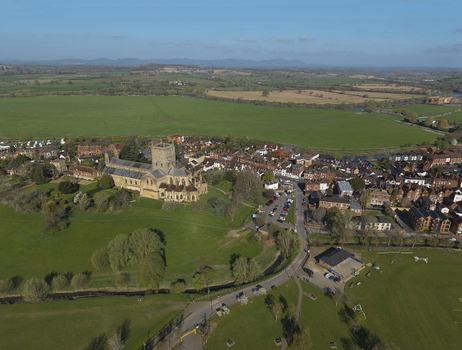 Aerial view of Tewkesbury Abbey surrounded by historic town buildings green meadows and winding rivers in Tewkesbury England United Kingdom.