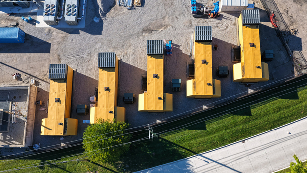 Aerial view of several large yellow industrial generator units arranged in a gravel yard next to a road and green grass in Southfield Michigan United States.