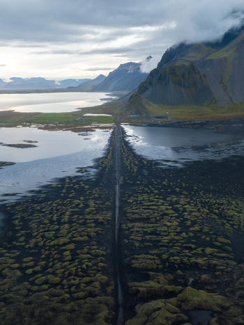 Aerial view of the stark black sands meeting the tranquil waters near Vestrahorn Mountain under a brooding sky Höfn Iceland. Aerial view of the stark black sands meeting the tranquil waters near Vestrahorn Mountain under a brooding sky Höfn Iceland.