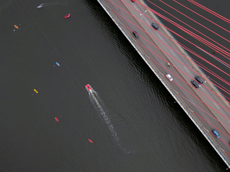 Aerial view of the cable stayed John Paul II Bridge over the Martwa Wisla river with cars driving on the deck and colorful kayaks paddling in the water below in Gdansk Poland. Aerial view of the cable stayed John Paul II Bridge over the Martwa Wisla river with cars driving on the deck and colorful kayaks paddling in the water below in Gdansk Poland.