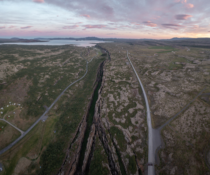 Aerial view of the Almannagja tectonic rift in Thingvellir National Park featuring lava fields mossy terrain and a road under a soft sunset sky in Selfoss Blaskogabyggd Iceland. Aerial view of the Almannagja tectonic rift in Thingvellir National Park featuring lava fields mossy terrain and a road under a soft sunset sky in Selfoss Blaskogabyggd Iceland.