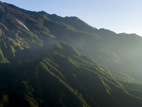 Aerial view of the lush green slopes of Mount Merapi near Bunker Kaliadem with morning sunlight and mist in Kecamatan Pakem Daerah Istimewa Yogya Indonesia. Aerial view of the lush green slopes of Mount Merapi near Bunker Kaliadem with morning sunlight and mist in Kecamatan Pakem Daerah Istimewa Yogya Indonesia.