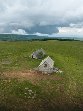 Aerial view of ancient stone buildings nestled in a vibrant green field under a dramatic cloudy sky Nasbinals Occitanie France. Aerial view of ancient stone buildings nestled in a vibrant green field under a dramatic cloudy sky Nasbinals Occitanie France.
