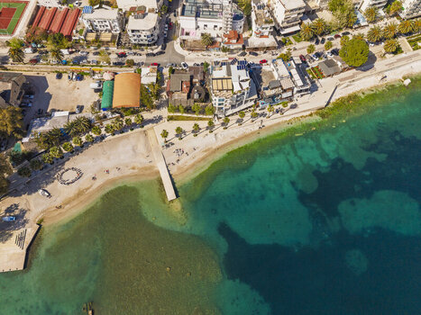 Aerial view of the Saranda coastline featuring a sandy beach a small pier extending into turquoise waters and urban buildings in Saranda Vlore County Albania. Aerial view of the Saranda coastline featuring a sandy beach a small pier extending into turquoise waters and urban buildings in Saranda Vlore County Albania.