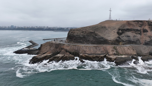 Aerial view of the coastal cliffs in Barranco with a prominent cross a winding road along the edge and crashing waves against the rocky shore in Barranco Lima Province Peru.