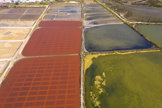 Aerial view of the Salinas do Grelha salt pans featuring vibrant red and green water basins separated by earthen paths in Olhao Faro Portugal. Aerial view of the Salinas do Grelha salt pans featuring vibrant red and green water basins separated by earthen paths in Olhao Faro Portugal.
