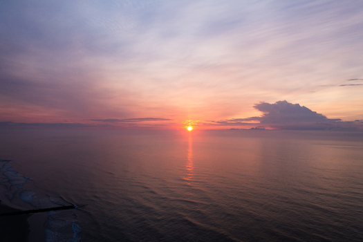Aerial view of Sea Isle City Beach at sunrise with calm ocean waters a sandy shoreline and a jetty under a soft pink and orange sky in Sea Isle City New Jersey United States.