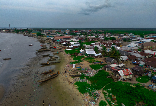Aerial view of Bonny Island featuring a coastal settlement with wooden fishing boats moored along the muddy shoreline and residential rooftops in Bonny Town Rivers Nigeria. Aerial view of Bonny Island featuring a coastal settlement with wooden fishing boats moored along the muddy shoreline and residential rooftops in Bonny Town Rivers Nigeria.