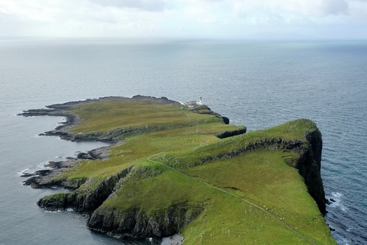 Aerial view of Neist Point Lighthouse situated on a dramatic grassy cliff edge overlooking the sea on the Isle of Skye Scotland United Kingdom.