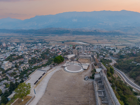 Aerial view of Gjirokaster Fortress with historic stone walls open air stage and clock tower overlooking the city and mountains at sunset Gjirokaster Gjirokaster County Albania. Aerial view of Gjirokaster Fortress with historic stone walls open air stage and clock tower overlooking the city and mountains at sunset Gjirokaster Gjirokaster County Albania.