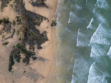 Aerial view of Godrevy Beach featuring dark jagged rocks and golden sand meeting turquoise ocean waves in Gwithian England United Kingdom. Aerial view of Godrevy Beach featuring dark jagged rocks and golden sand meeting turquoise ocean waves in Gwithian England United Kingdom.