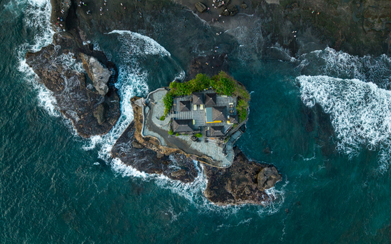 Aerial view of Tanah Lot Temple surrounded by dark volcanic rock formations and crashing ocean waves in Kecamatan Kediri Bali Indonesia. Aerial view of Tanah Lot Temple surrounded by dark volcanic rock formations and crashing ocean waves in Kecamatan Kediri Bali Indonesia.