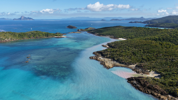 Aerial view of the turquoise waters and rocky coastline of Chance Bay surrounded by lush green vegetation in the Whitsundays Queensland Australia. Aerial view of the turquoise waters and rocky coastline of Chance Bay surrounded by lush green vegetation in the Whitsundays Queensland Australia.