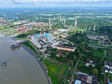 Aerial view of the Karnaphuli River with a large power plant facility industrial infrastructure and cargo ships docked along the riverbank in Chattogram Chittagong Division Bangladesh.