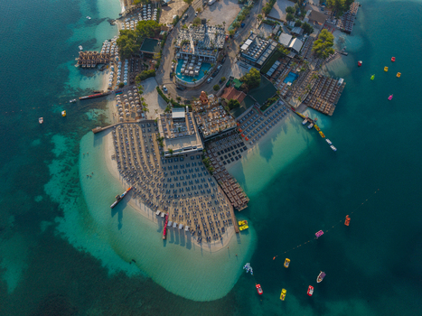 Aerial view of the coastal resort of Ksamil with turquoise waters sandy beaches rows of sun loungers and small boats in Ksamil Vlore County Albania. Aerial view of the coastal resort of Ksamil with turquoise waters sandy beaches rows of sun loungers and small boats in Ksamil Vlore County Albania.