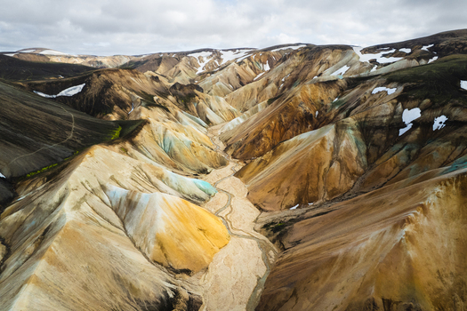 Aerial view of Landmannalaugar rhyolite mountains with colorful slopes a winding river valley and patches of snow under a cloudy sky Rangarthing ytra Iceland. Aerial view of Landmannalaugar rhyolite mountains with colorful slopes a winding river valley and patches of snow under a cloudy sky Rangarthing ytra Iceland.