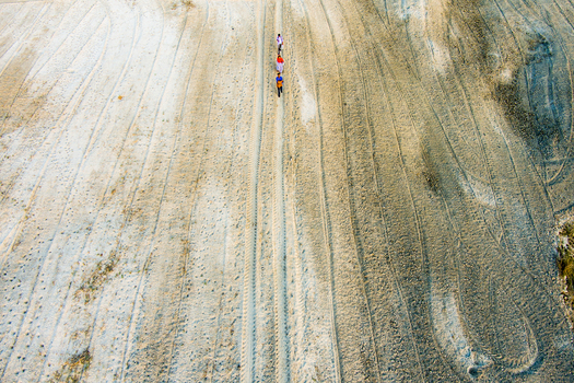 Aerial view of three people walking across a vast sandy riverbed marked with numerous tire tracks in Rajshahi Rajshahi Division Bangladesh.