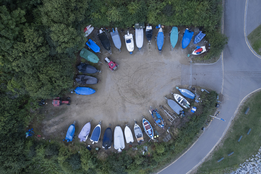 Aerial view of small boats parked in a semi circular arrangement on a gravel lot surrounded by lush trees and a nearby road in Runswick Bay England United Kingdom.