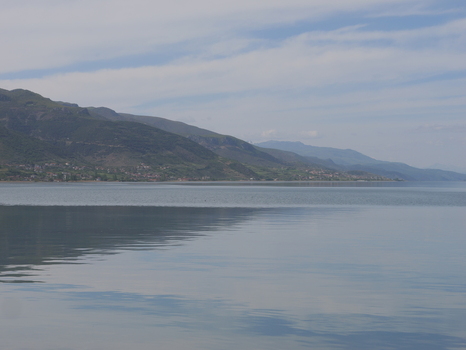 View of Lake Ohrid with mountains in the background under a blue sky with light clouds in Pogradec Korce County Albania. View of Lake Ohrid with mountains in the background under a blue sky with light clouds in Pogradec Korce County Albania.