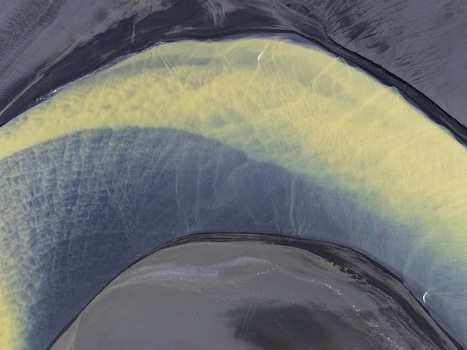 Aerial view of the abstract patterns of a glacial river with yellow sediment mixing with blue water over dark volcanic sand in Hallgeirseyjarvegur Rangarthing eystra Iceland. Aerial view of the abstract patterns of a glacial river with yellow sediment mixing with blue water over dark volcanic sand in Hallgeirseyjarvegur Rangarthing eystra Iceland.