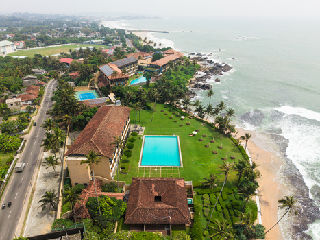 Aerial view of a luxury coastal resort with a swimming pool and palm trees along the sandy beach and ocean in Galle Southern Province Sri Lanka. Aerial view of a luxury coastal resort with a swimming pool and palm trees along the sandy beach and ocean in Galle Southern Province Sri Lanka.