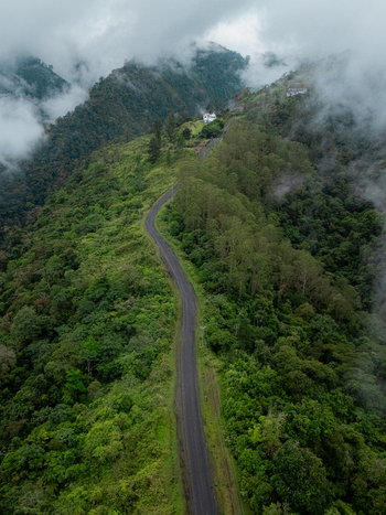 Aerial view of a winding mountain road on a lush green ridge surrounded by dense tropical forest and low hanging clouds in Cinchona Alajuela Province Costa Rica. Aerial view of a winding mountain road on a lush green ridge surrounded by dense tropical forest and low hanging clouds in Cinchona Alajuela Province Costa Rica.