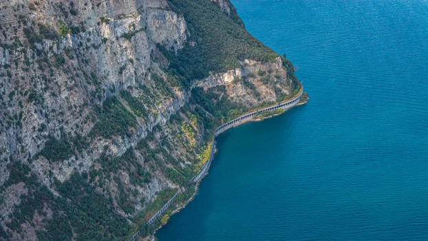 Aerial view of the scenic coastal road carved into steep limestone cliffs along the turquoise waters of Lake Garda Italy.