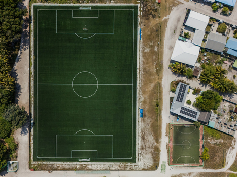 Aerial view of a vibrant green football field contrasting with the sandy surroundings and nearby buildings Vashafaru Island Thiladhummathi Atoll Maldives.