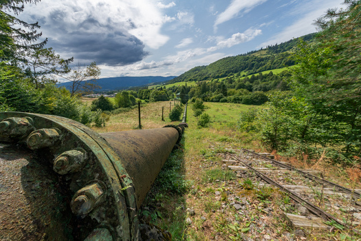 View of the Jasenie Hydroelectric Power Plant penstock on a grassy hillside with old railway tracks surrounded by trees and mountains in Jasenie Banska Bystrica Regio Slovakia.