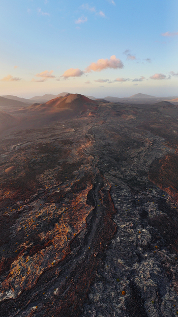 Aerial view of the volcanic landscape featuring dark lava fields craters and rugged terrain illuminated by the warm light of the setting sun Lanzarote. Aerial view of the volcanic landscape featuring dark lava fields craters and rugged terrain illuminated by the warm light of the setting sun Lanzarote.