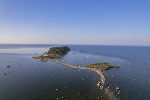 Aerial view of Kuradi saar a small forested island connected by a narrow sandbar in the Baltic Sea surrounded by calm water and scattered boulders in Kasmu Laane Viru County Estonia.