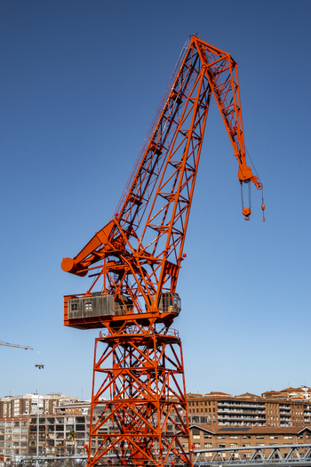 View of the historic red Carola Crane standing tall against a clear blue sky with urban buildings in the background Greater Bilbao Basque Country Spain. View of the historic red Carola Crane standing tall against a clear blue sky with urban buildings in the background Greater Bilbao Basque Country Spain.