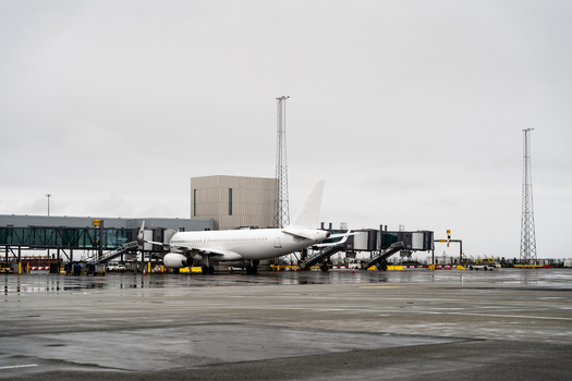 View of a white passenger airplane parked at an airport gate on a wet tarmac under an overcast sky in Iceland. View of a white passenger airplane parked at an airport gate on a wet tarmac under an overcast sky in Iceland.